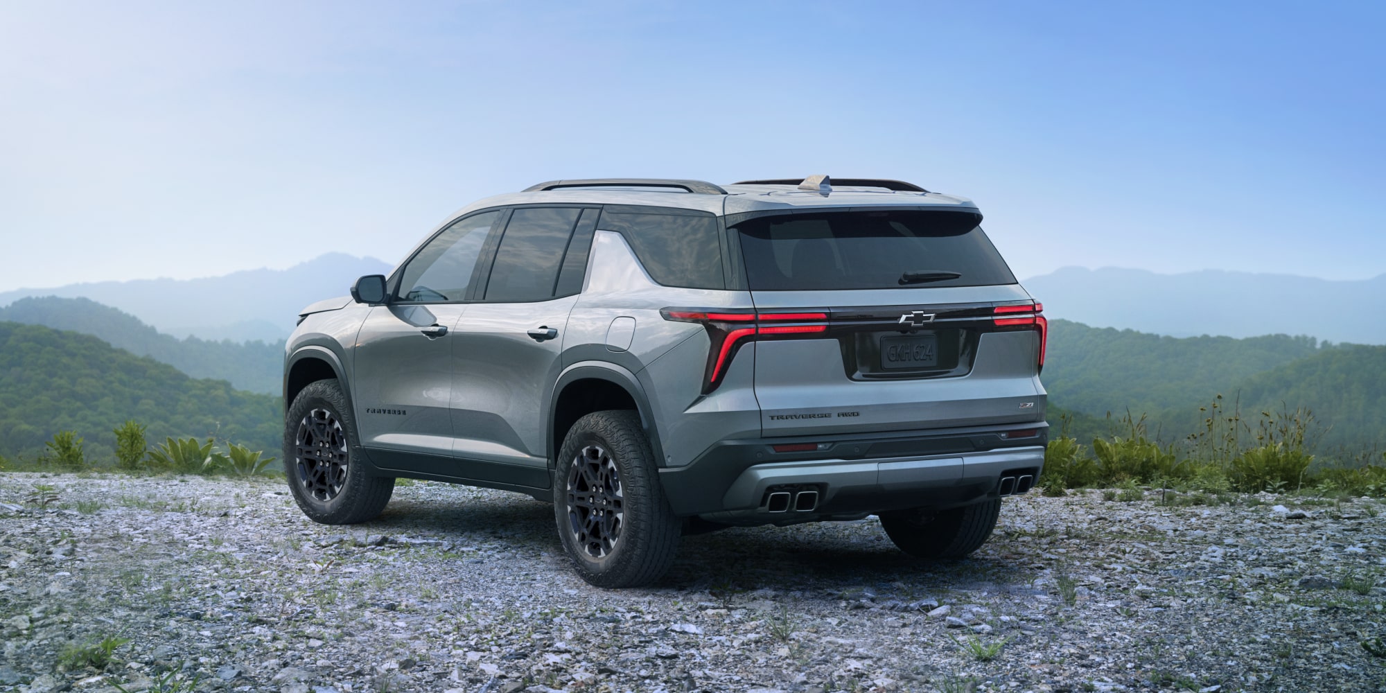 A 2027 Chevy Traverse Parked at a Scenic Overlook With Mountain Views Visible From a Rear Three-Quarter Angle.