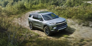 A 2027 Chevy Traverse Driving Along a Dirt Road Through a Natural Landscape Showcasing Rugged SUV Styling and Adventure-Ready Capability.