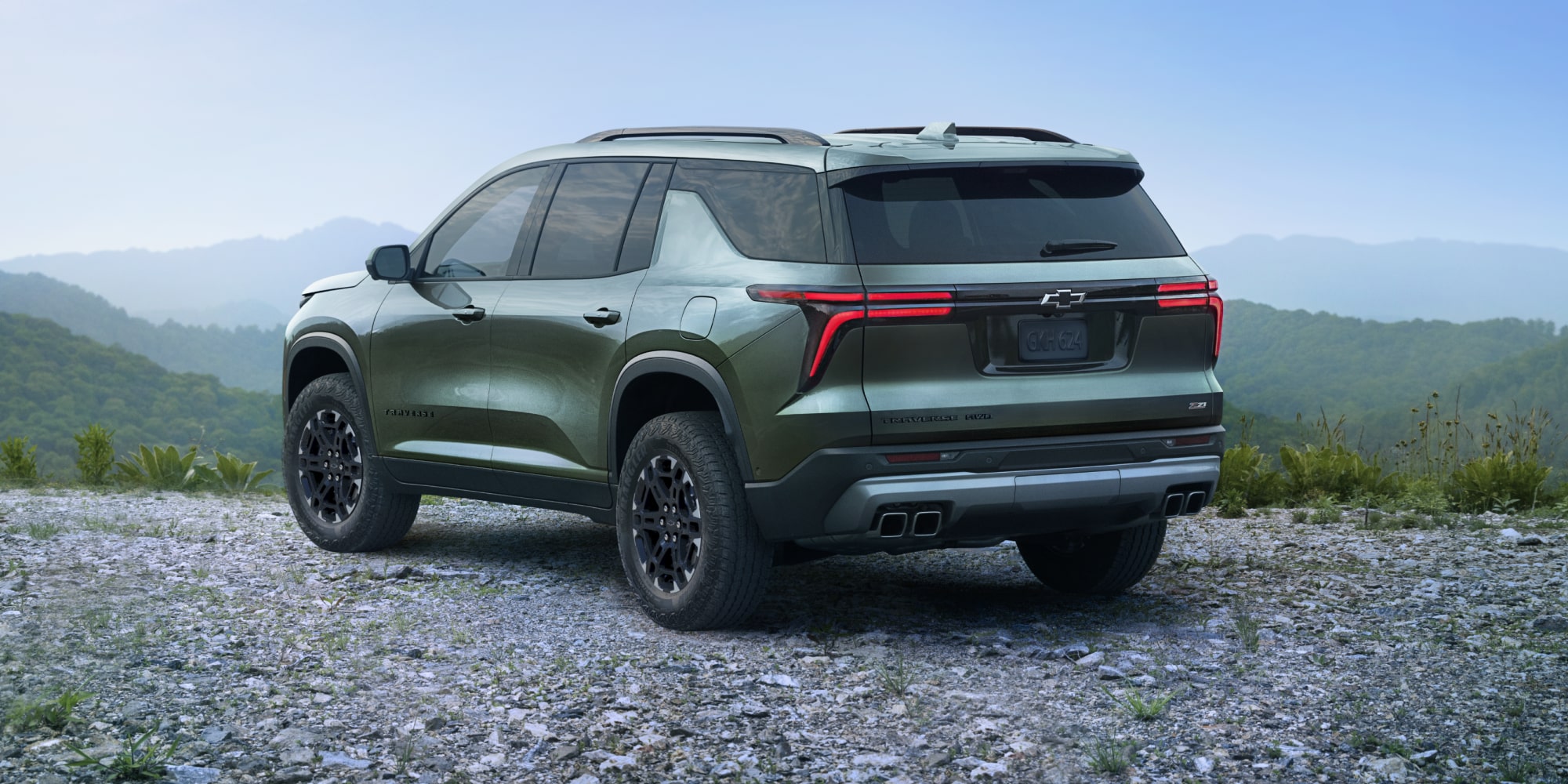 A 2027 Chevy Traverse Parked at a Scenic Overlook With Mountain Views Visible From a Rear Three-Quarter Angle.