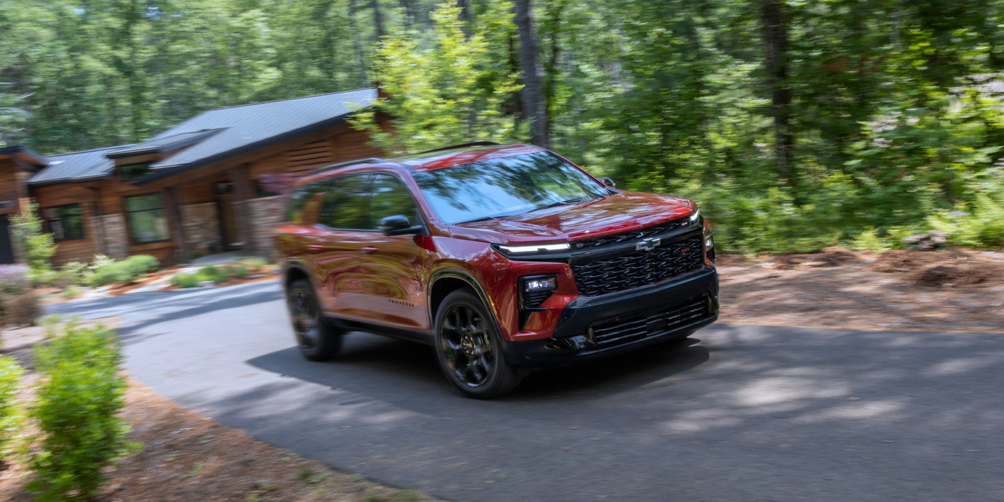 Three-quarter, Motion View of a Red 2027 Chevy Traverse Driving Down a Cabin Driveway