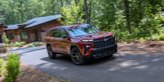 Three-quarter, Motion View of a Red 2027 Chevy Traverse Driving Down a Cabin Driveway