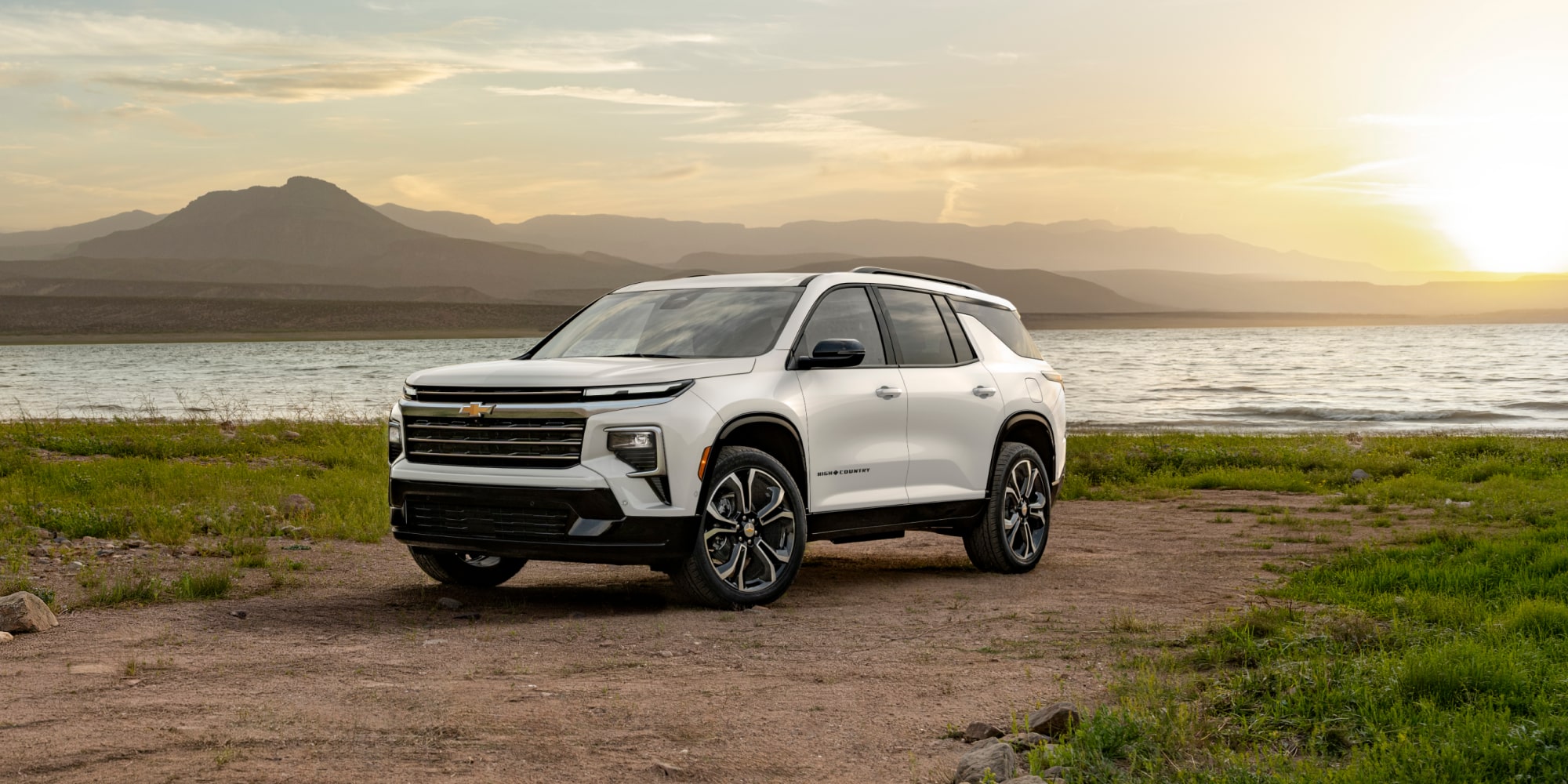 A White 2027 Chevy Traverse Parked by a Lake During a Sunrise Over the Mountains