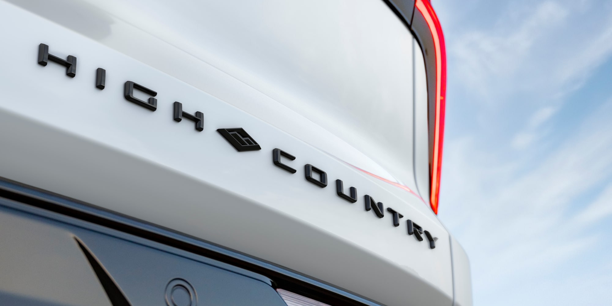 Close-up of a White 2027 Chevy Traverse Trim Plate Reading "High Country" on the Exterior of the Vehicle