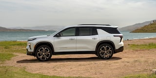 A Profile View of a White 2027 Chevy Traverse Parked on a Dirt Patch Next to a Lake