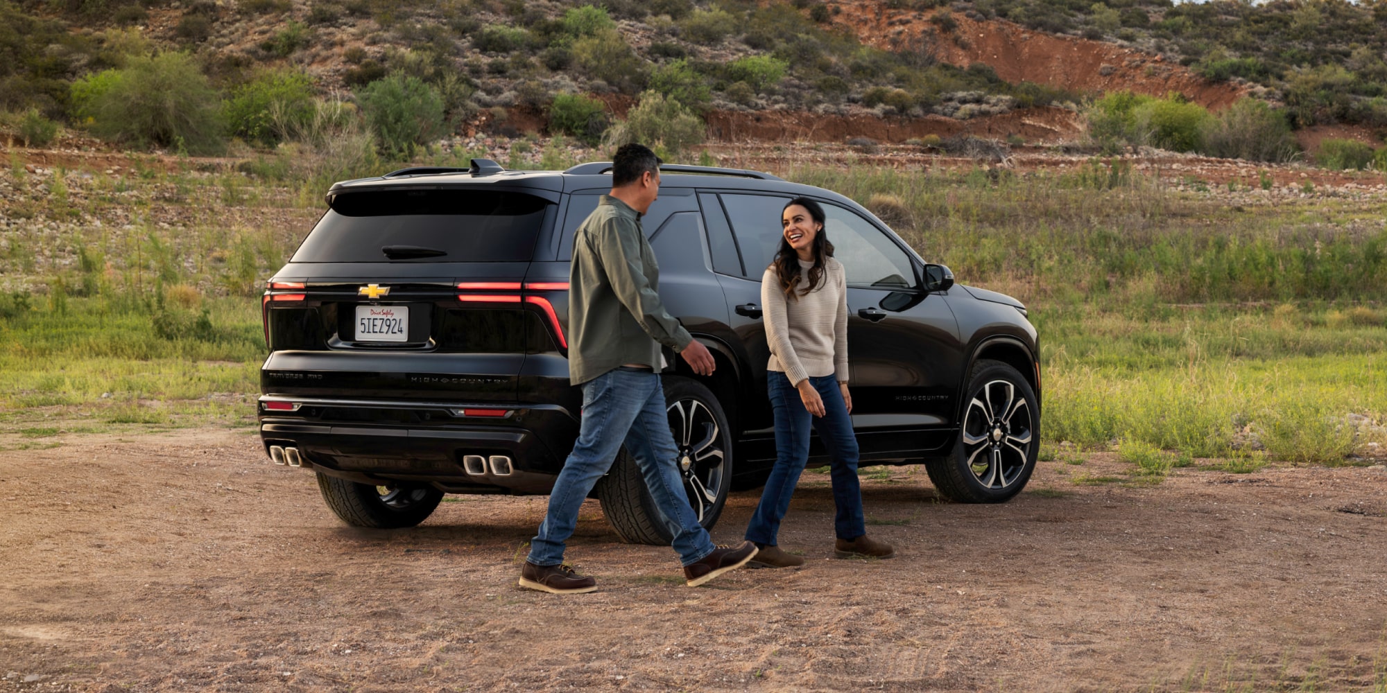 A Couple Walking From a Parked Black 2027 Chevy Traverse in the Terrain