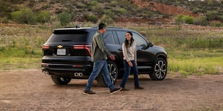 A Couple Walking From a Parked Black 2027 Chevy Traverse in the Terrain