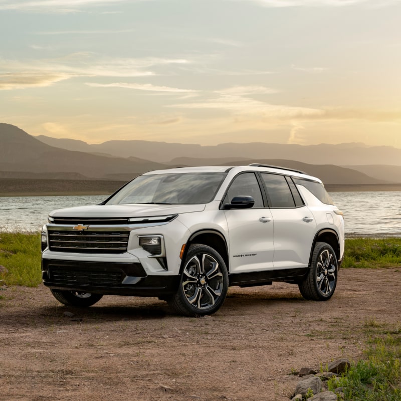 A White 2027 Chevy Traverse Parked by a Lake During a Sunrise Over the Mountains