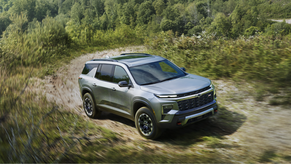 A 2027 Chevy Traverse Driving Along a Dirt Road Through a Natural Landscape.