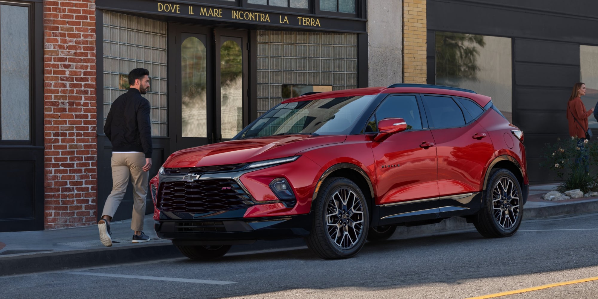 A Man Walking Toward His Red Chevy Blazer Parked in Front of a Modern Building