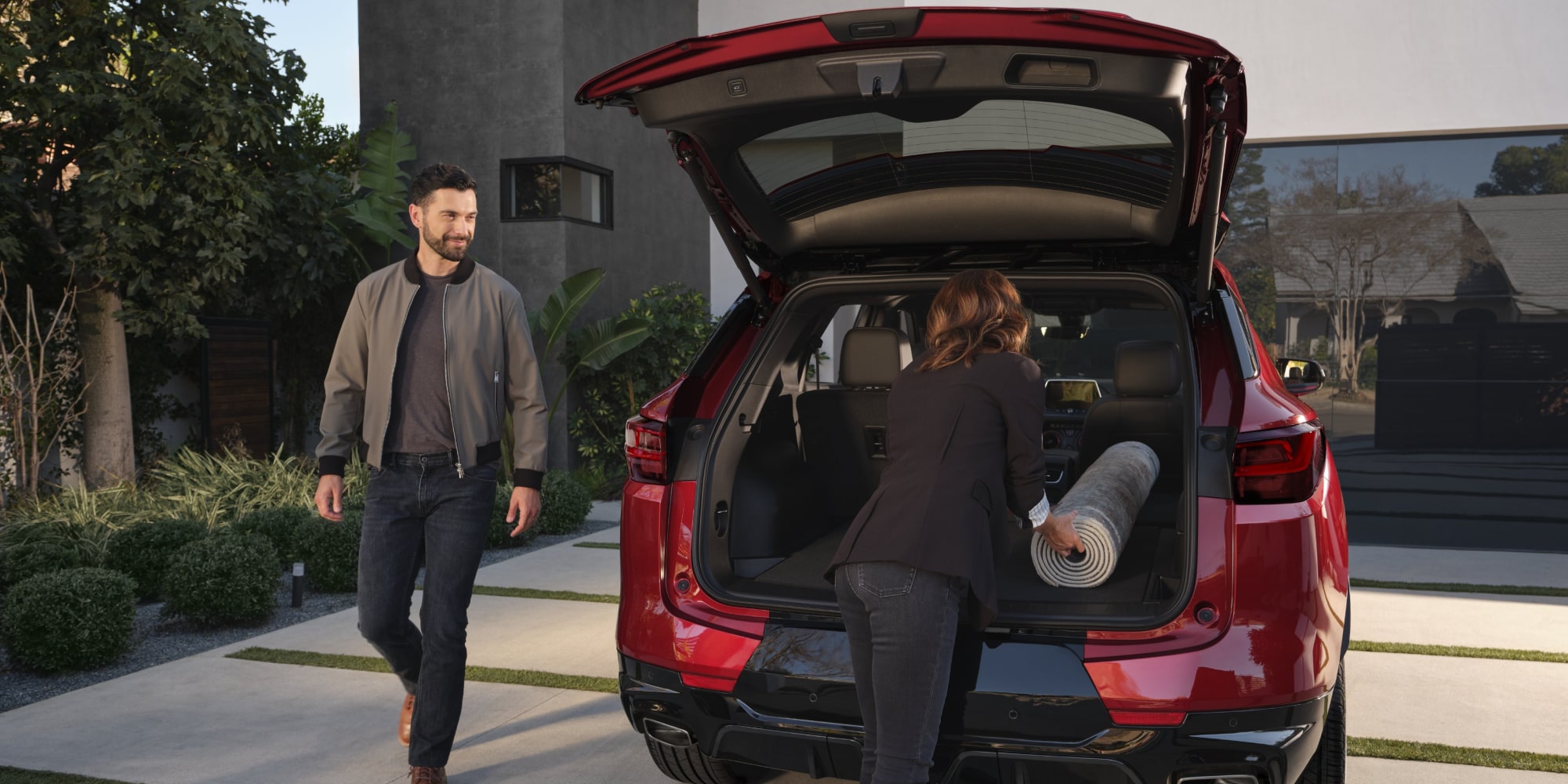 A Woman Putting a Mat Inside the Trunk of a Red Chevy Blazer While a Smiling Man Walks Toward Her