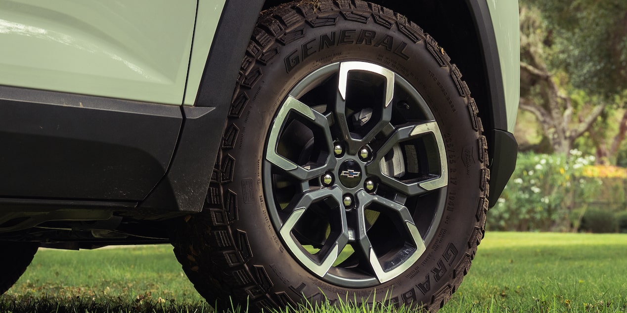 A Close-Up View of a Chevrolet Equinox Wheel Featuring Black and Silver Alloy Rims and All-Terrain Tires Parked on Green Grass.