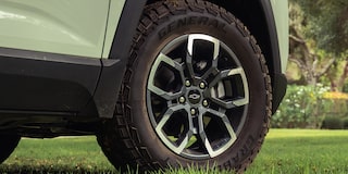 A Close-Up View of a Chevrolet Equinox Wheel Featuring Black and Silver Alloy Rims and All-Terrain Tires Parked on Green Grass.