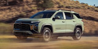 A Green Chevrolet Equinox Driving Across a Sunlit Dirt Landscape With Rolling Hills and Brush in the Background.