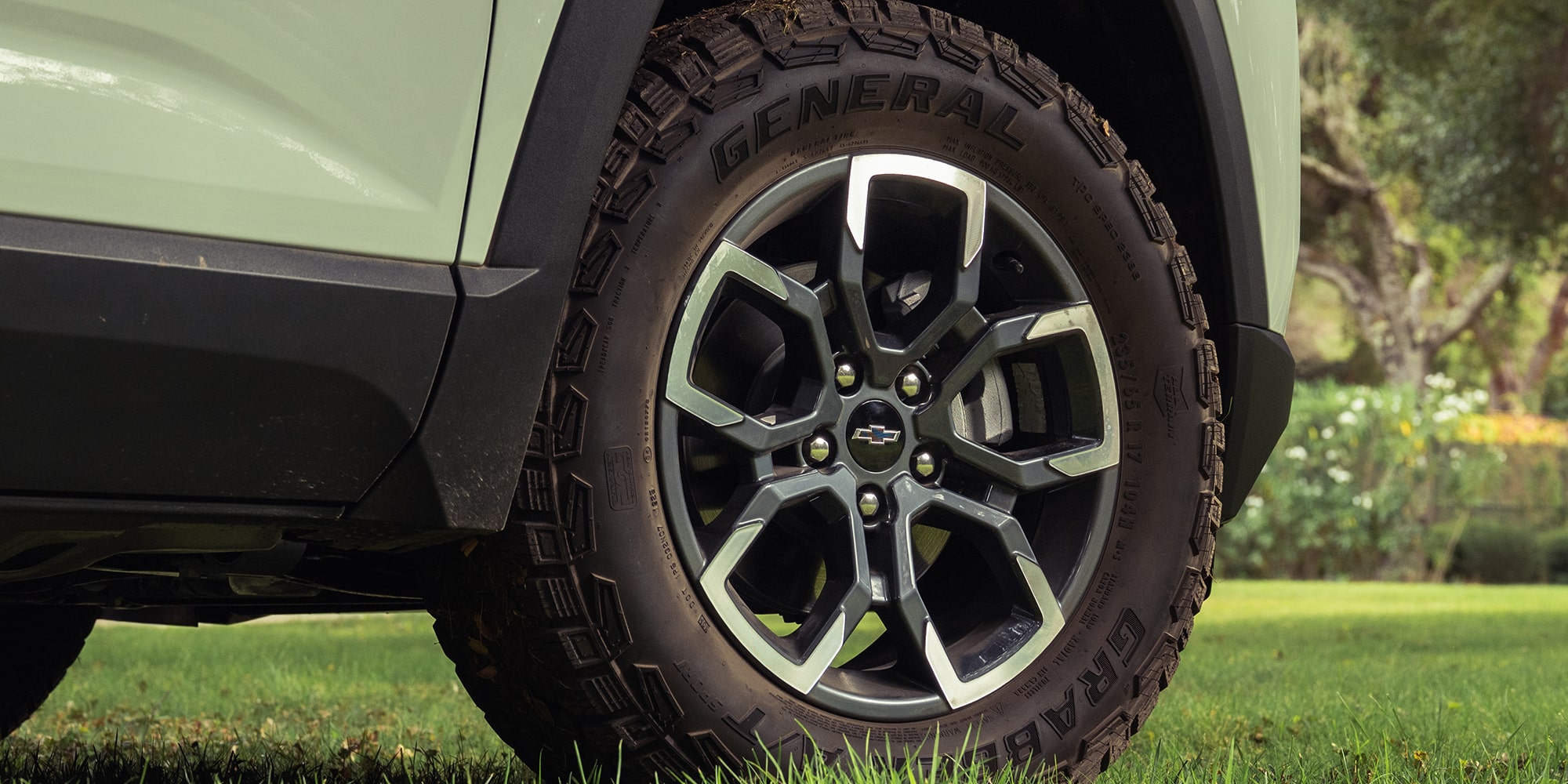 A Close-Up View of a Chevrolet Equinox Wheel Featuring Black and Silver Alloy Rims and All-Terrain Tires Parked on Green Grass.