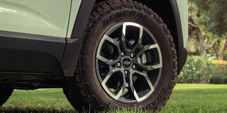 A Close-Up View of a Chevrolet Equinox Wheel Featuring Black and Silver Alloy Rims and All-Terrain Tires Parked on Green Grass.