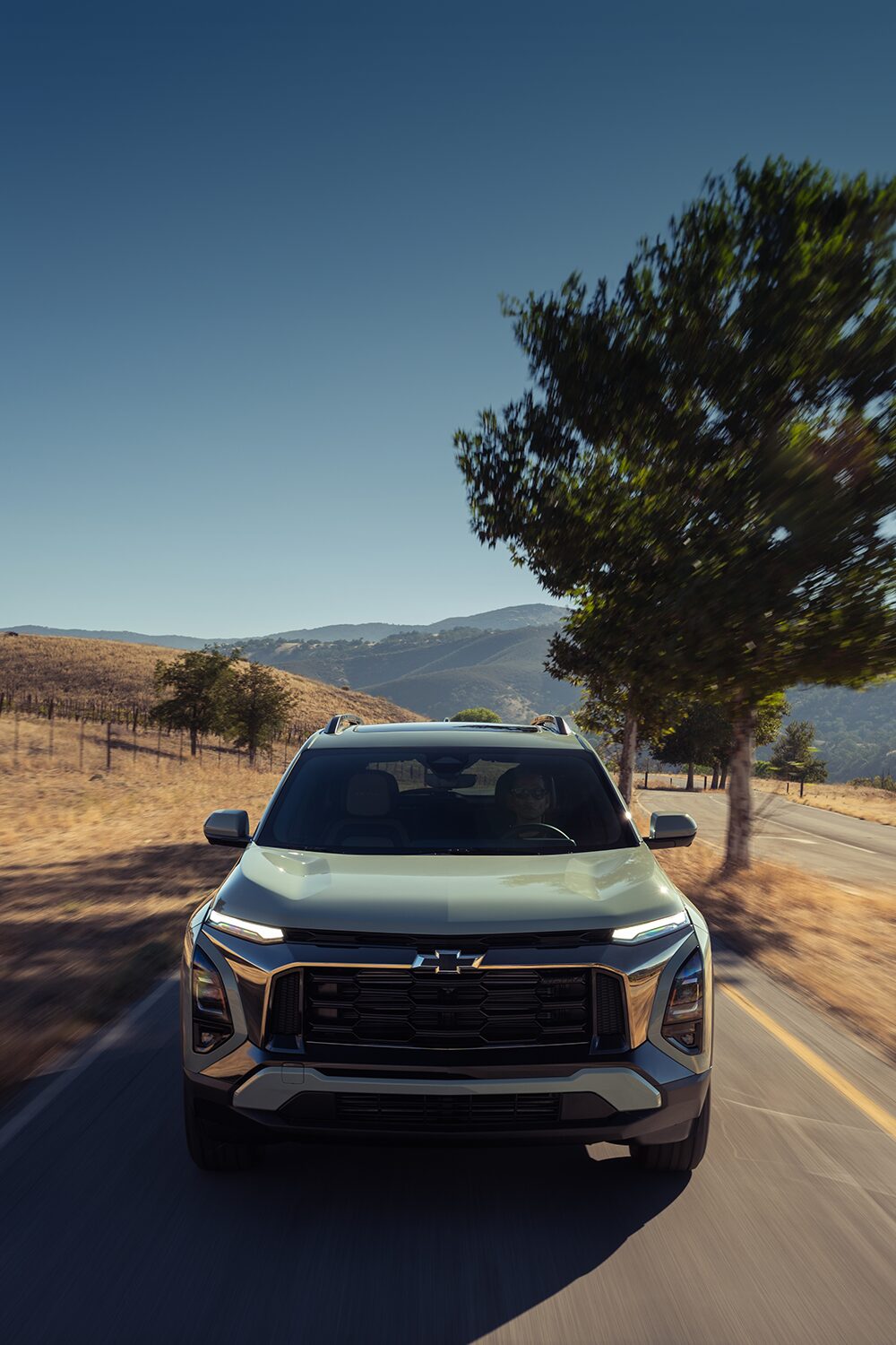 A Chevrolet Equinox Driving Down a Rural Road With Dry Grass and Trees Under a Clear Blue Sky.
