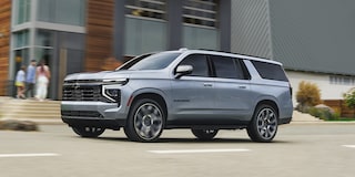 A Silver Chevrolet Suburban Driving Through an Urban Area Past Modern Buildings and Storefronts.