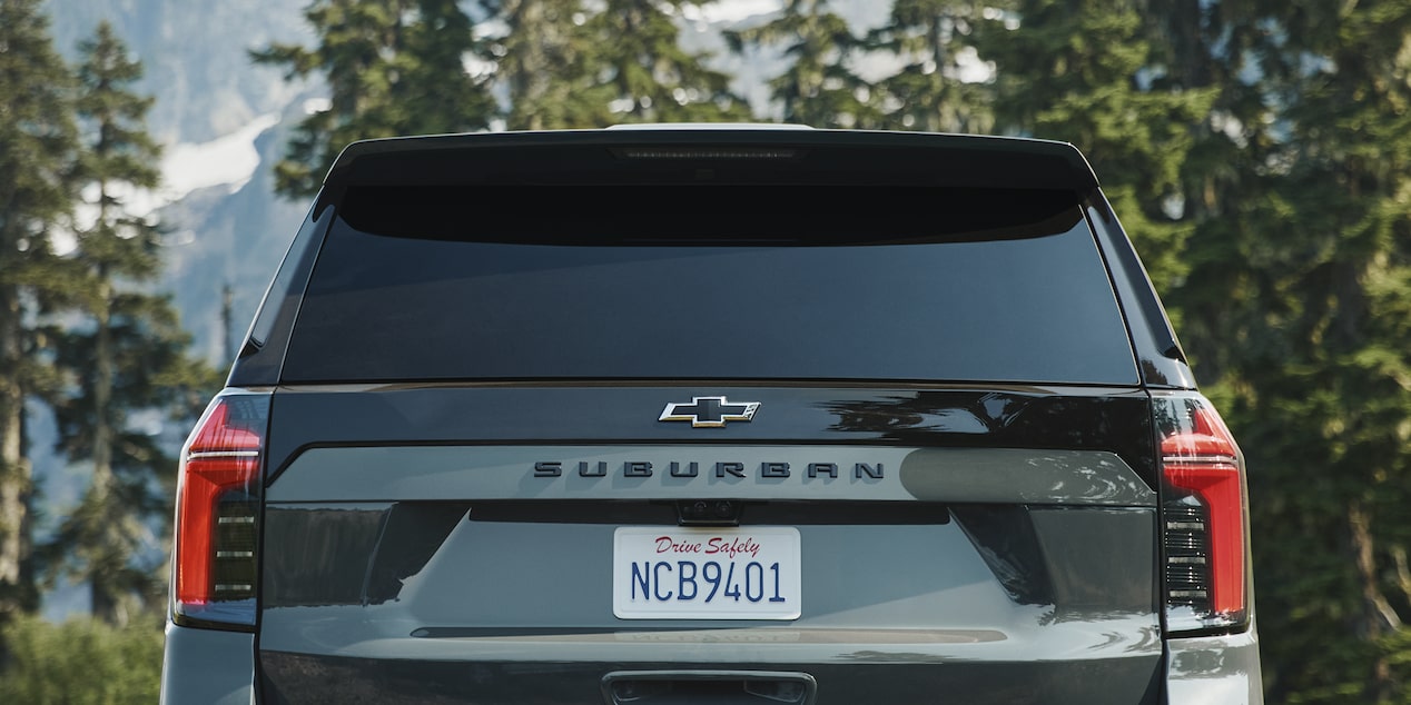 The Rear of a Black Chevrolet Suburban Showing the Suburban Badge, Vertical LED Taillights, and a Visible License Plate Against a Forested Mountain Backdrop.