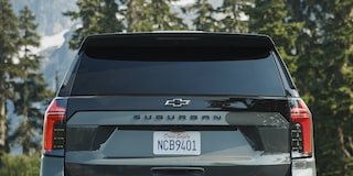 The Rear of a Black Chevrolet Suburban Showing the Suburban Badge, Vertical LED Taillights, and a Visible License Plate Against a Forested Mountain Backdrop.