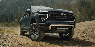 A Black Chevrolet Suburban Driving Uphill on a Rocky Dirt Trail With Evergreen Trees and Steep Terrain Surrounding the Vehicle.