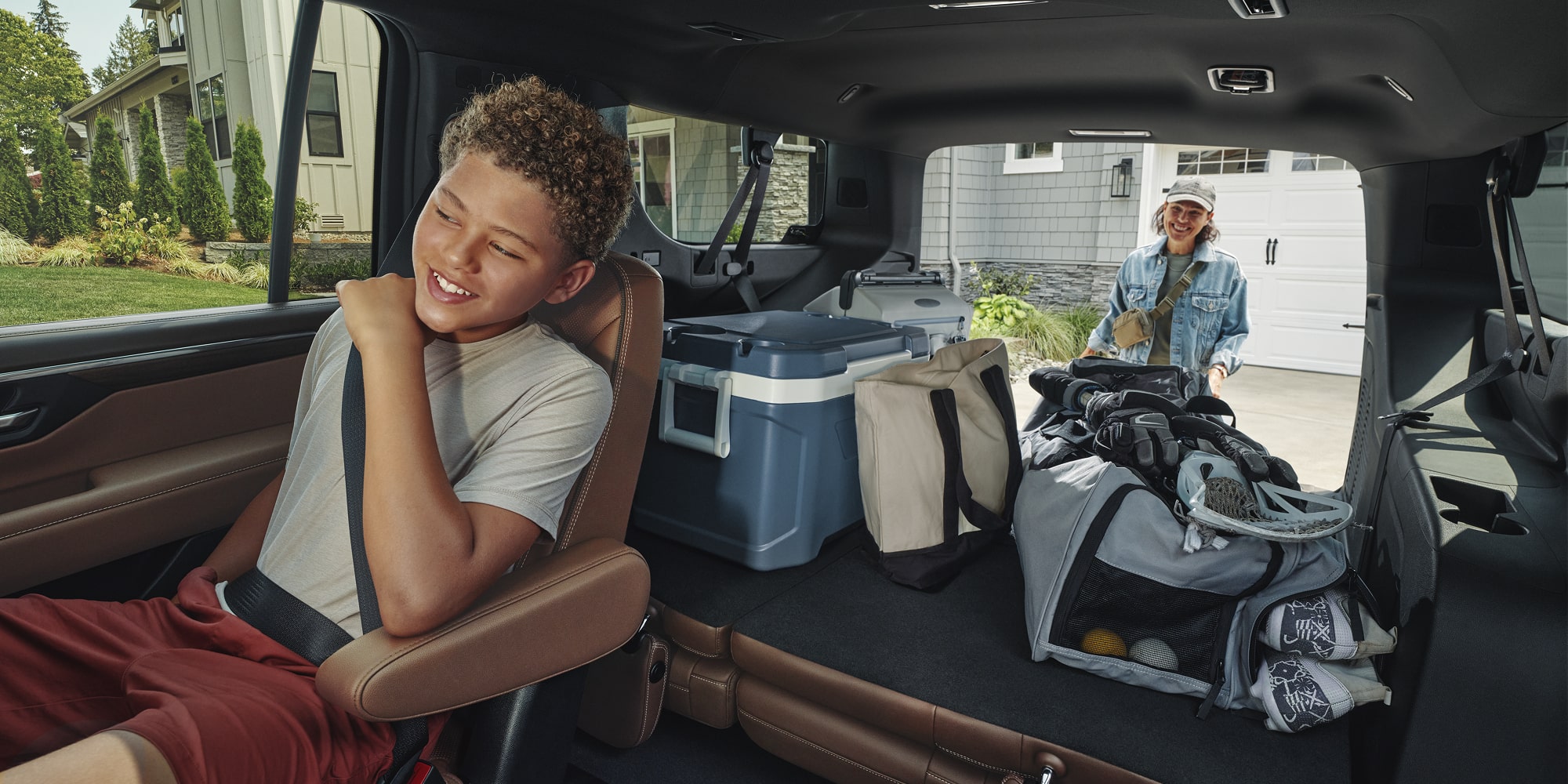 The Rear Cabin of a Chevrolet Suburban With a Child Passenger Relaxing While Cargo and Gear Are Organized Beside Them.