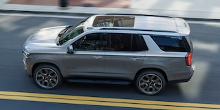 A White and Black Chevrolet Tahoe Driving on a Two-Lane Road Beside a Dense Evergreen Forest.