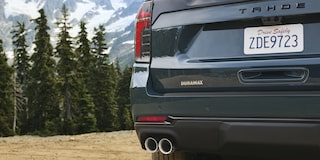 The Rear of a Chevrolet Tahoe Showing Dual Exhaust Outlets, a Tahoe Badge, and a Visible License Plate Against a Forest Backdrop.