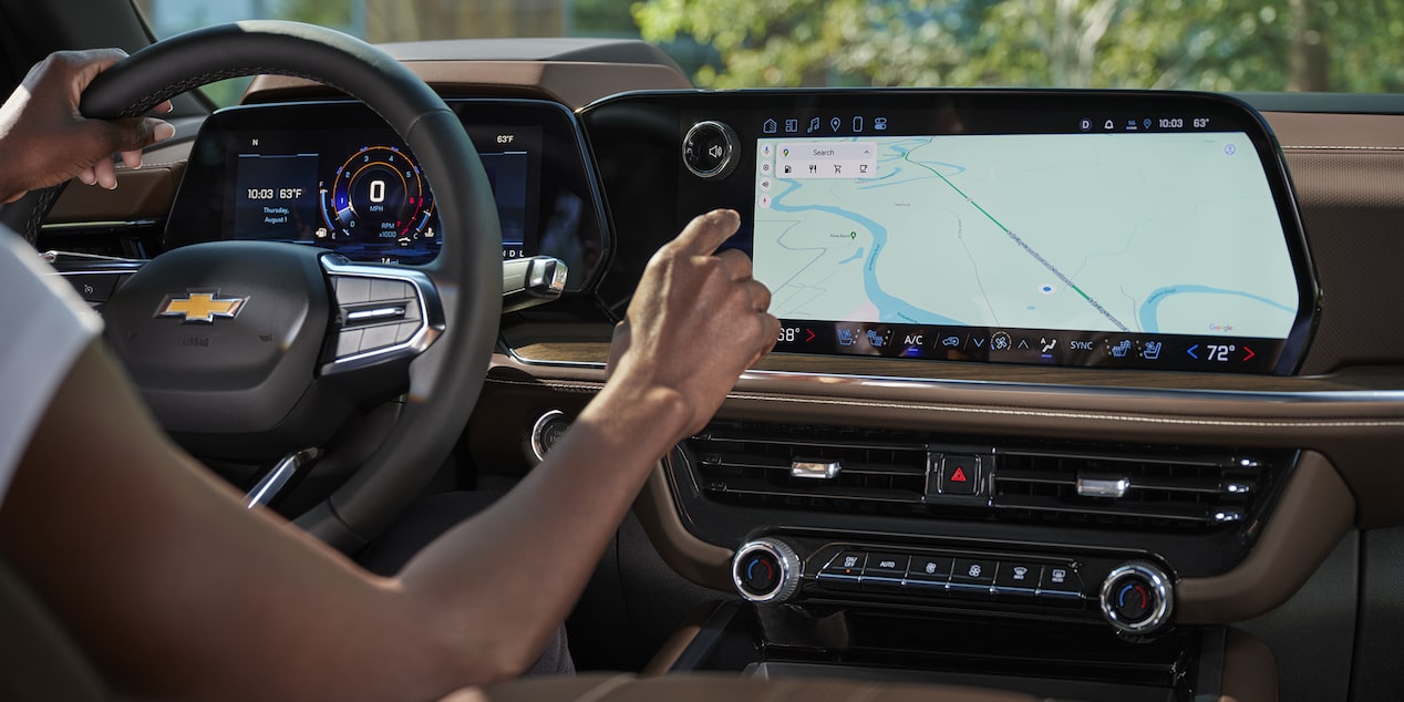 A Driver Inside a Chevrolet Tahoe Using the Large Central Touchscreen Display While Navigating a Map Interface.