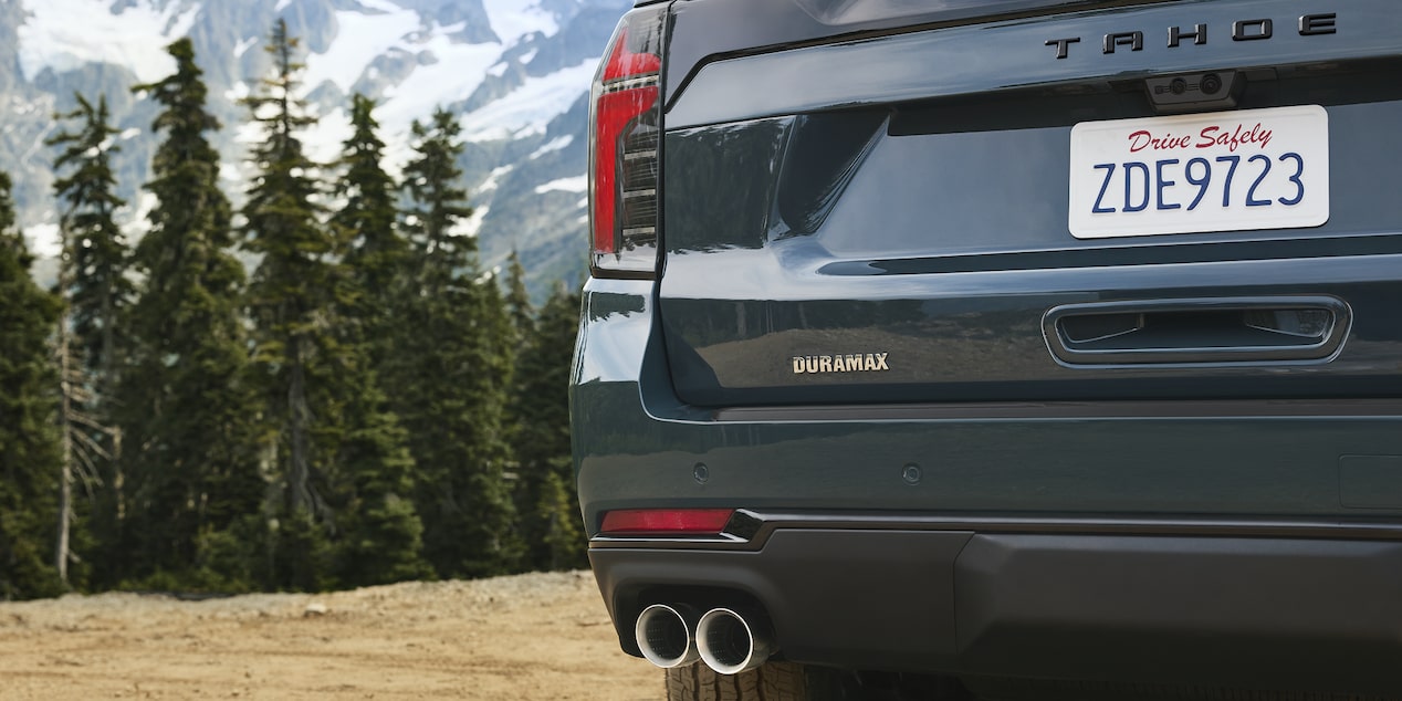 The Rear of a Chevrolet Tahoe Showing Dual Exhaust Outlets, a Tahoe Badge, and a Visible License Plate Against a Forest Backdrop.