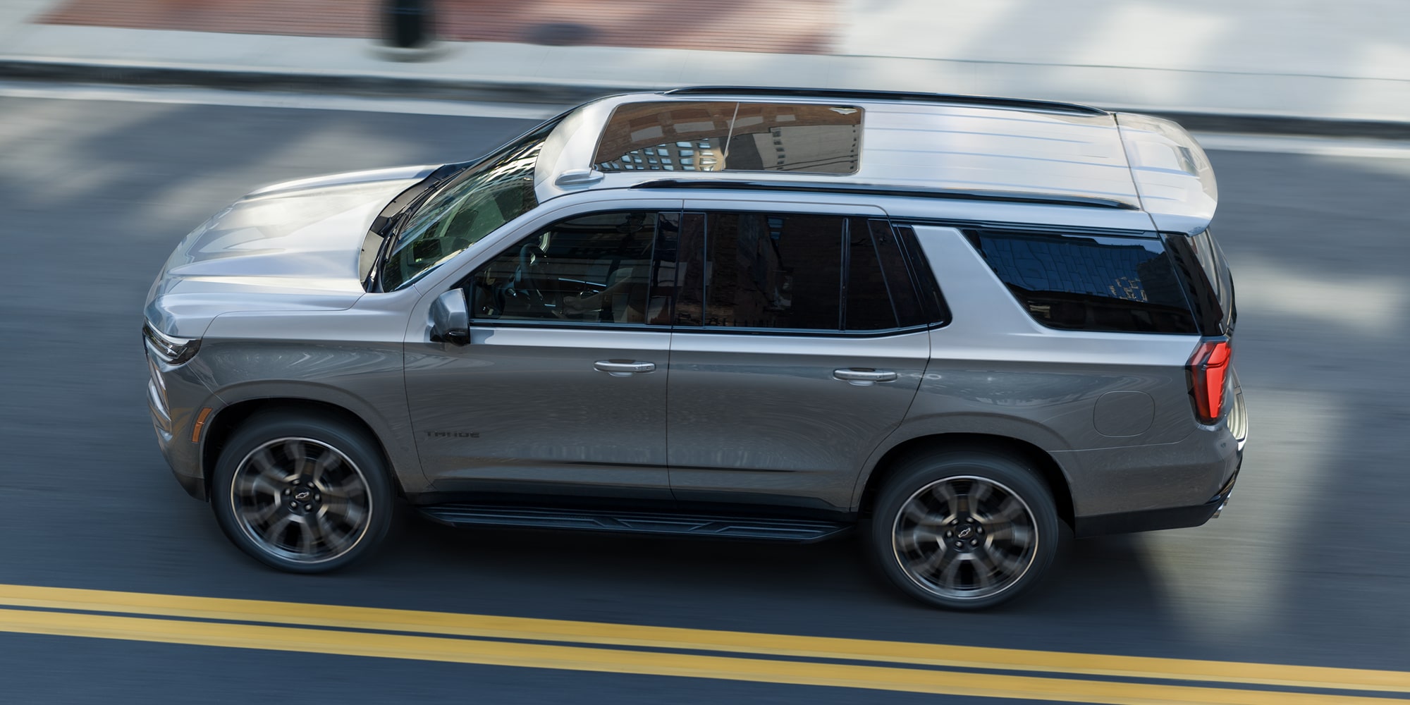 A White and Black Chevrolet Tahoe Driving on a Two-Lane Road Beside a Dense Evergreen Forest.