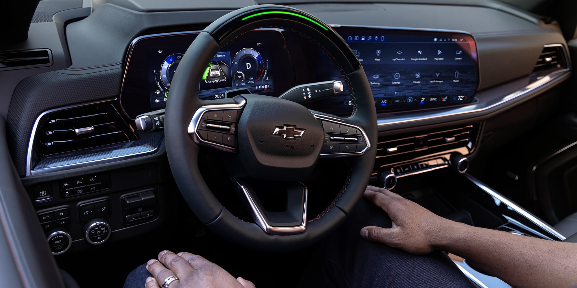 A Close-Up View of a Chevrolet Tahoe Steering Wheel and Illuminated Digital Driver Display With a Hand Resting on the Gear Selector.