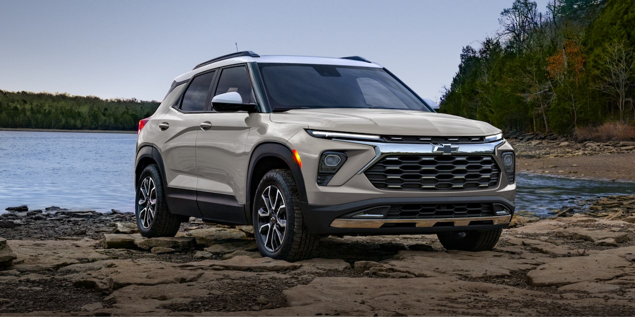 A Chevrolet Trailblazer Positioned on a Rocky Shoreline near a Calm Lake with Forest Trees in the Background.