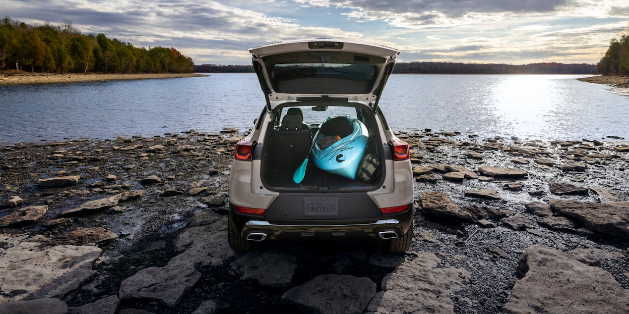 A Chevrolet Trailblazer with Its Rear Liftgate Open Revealing Kayaks and Gear as It Sits on a Rock-Lined Shore beside a Calm Lake.