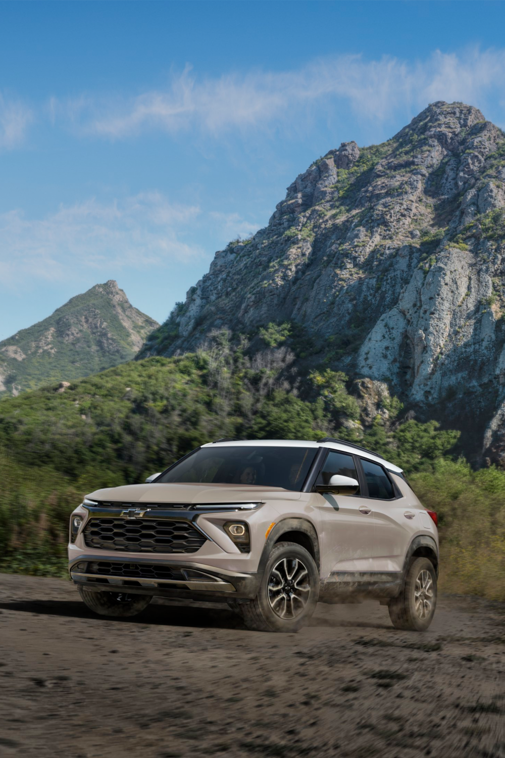 A Chevrolet Trailblazer Driving on a Dirt Mountain Road with Dust Kicking Up as It Passes Lush Greenery and Rocky Cliffs.