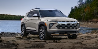 Una Chevrolet Trailblazer ubicada sobre una orilla rocosa junto a un lago tranquilo, con un bosque de árboles en el fondo.