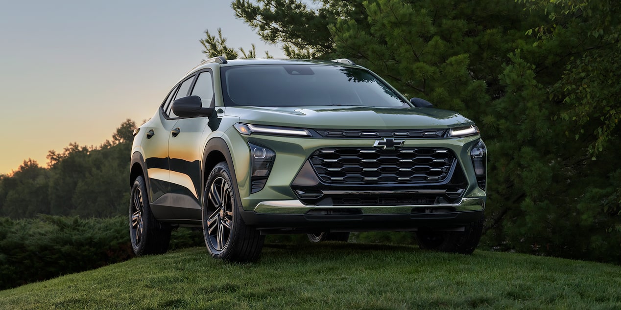 A Green Chevrolet Trax Parked on a Grassy Hill at Sunset With Dense Trees in the Background
