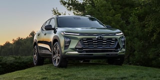 A Green Chevrolet Trax Parked on a Grassy Hill at Sunset With Dense Trees in the Background