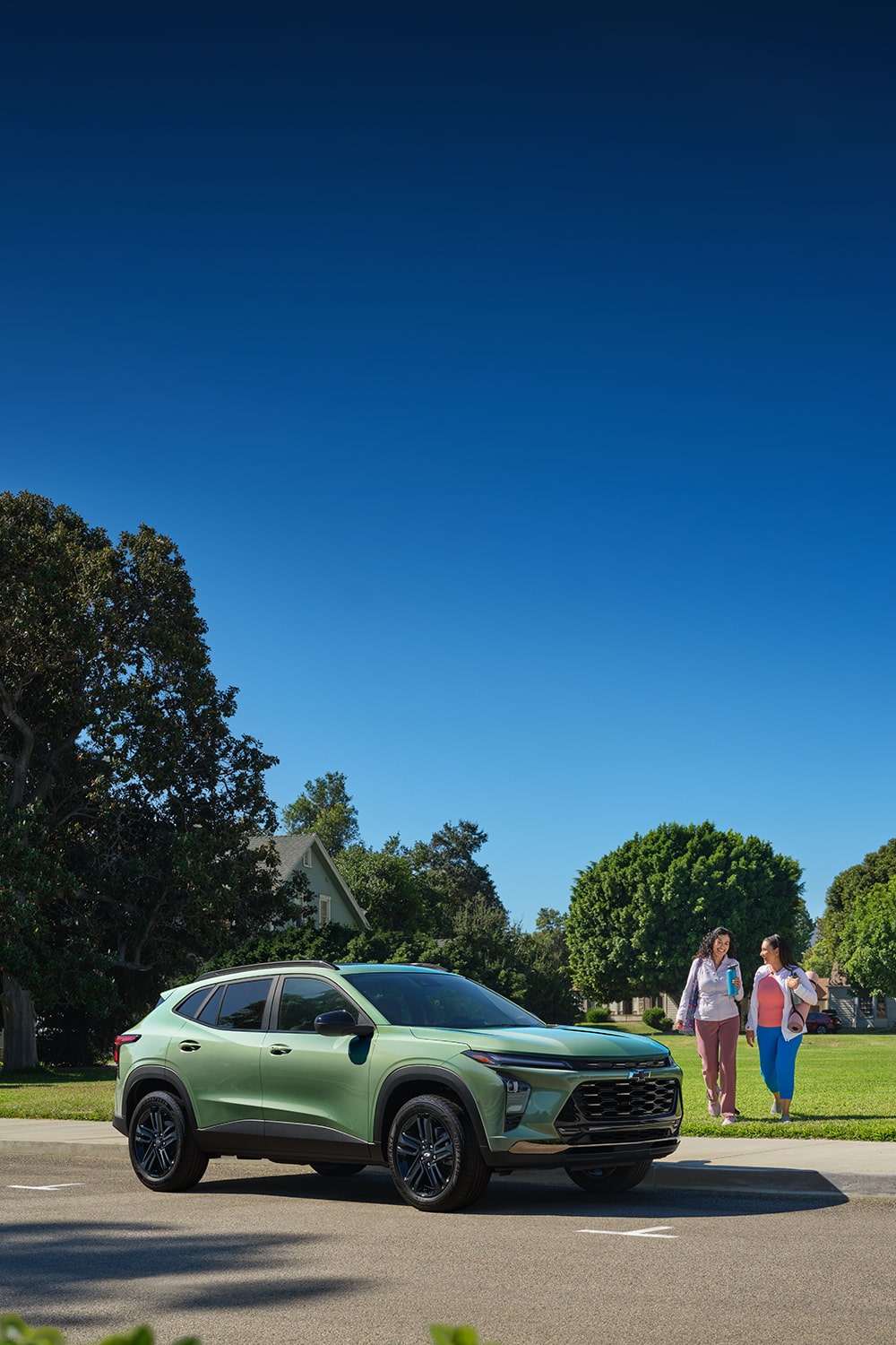 Chevy Trax Verde Claro estacionado cerca de un parque con dos mujeres caminando hacia el vehículo.