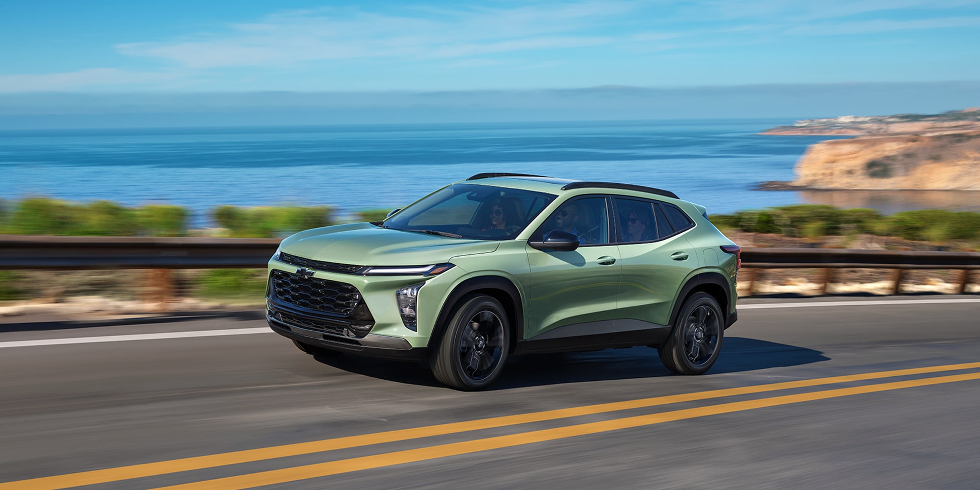Chevrolet Trax de color Verde Claro circulando por una carretera costera con olas del océano y acantilados rocosos al fondo.