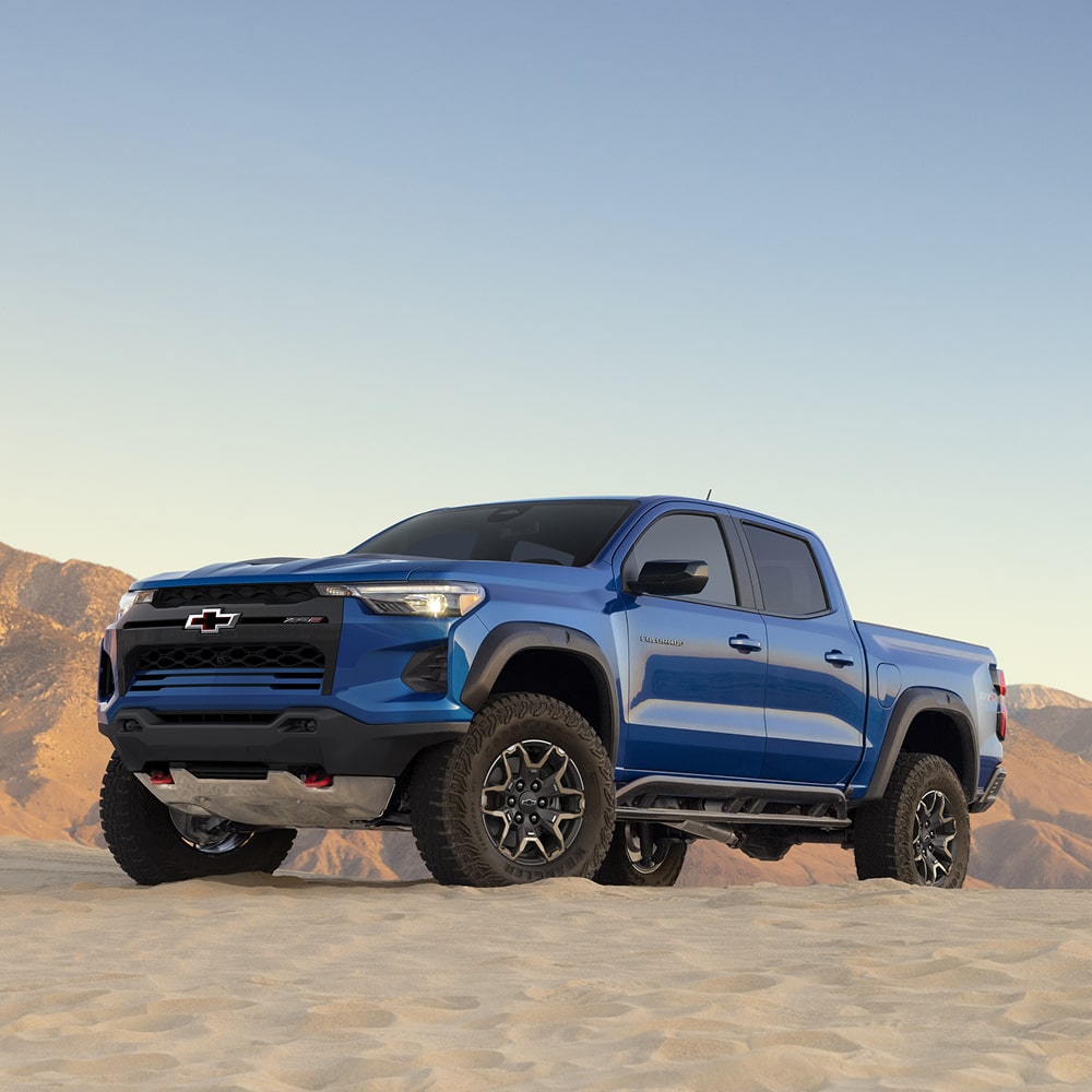 A Blue 2026 Chevrolet Colorado Parked on a Dirt Surface With Mountains in the Background.