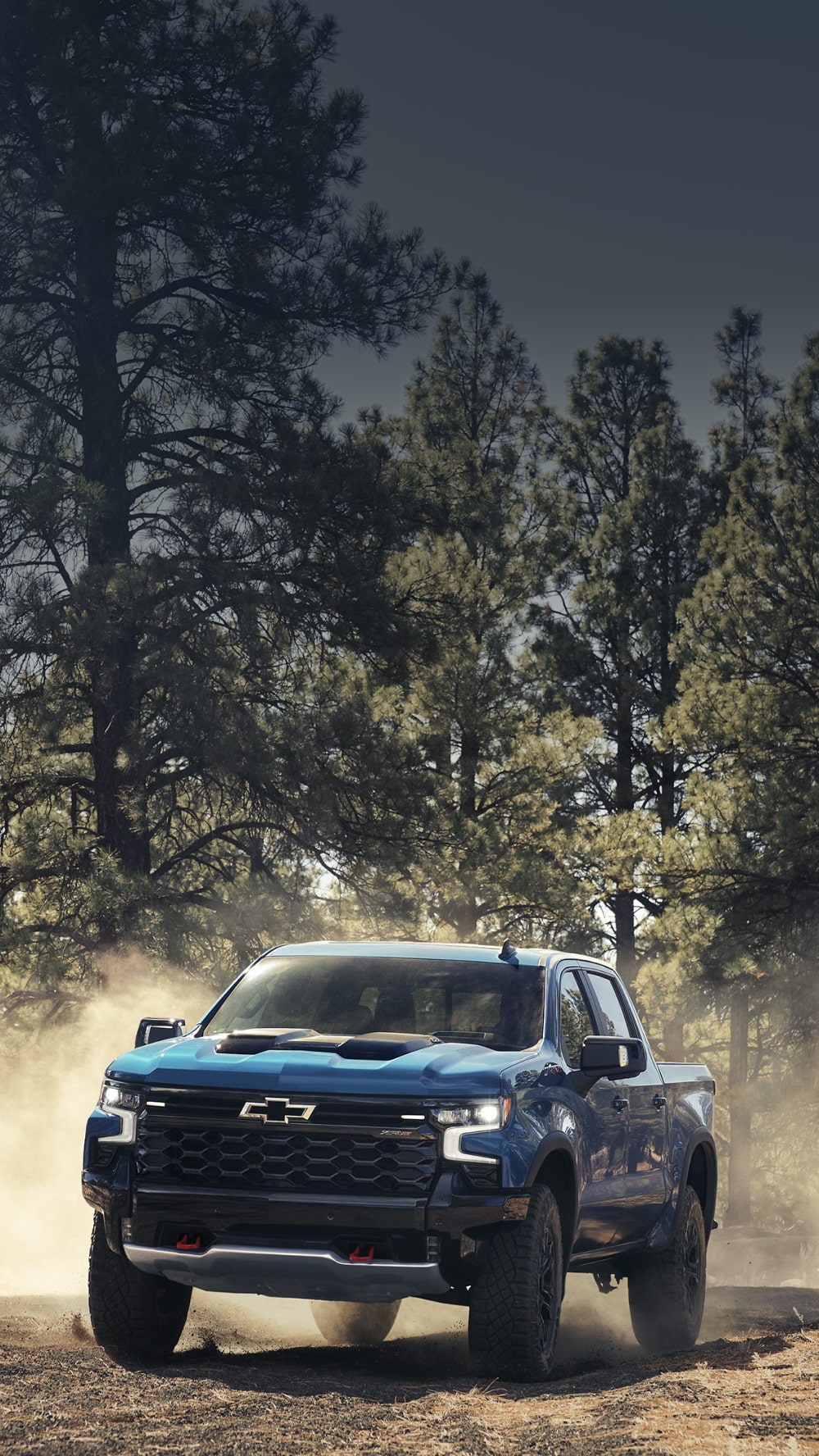Blue 2026 Chevy Silverado LD Driving on a Dirt Road in a Forested Area Kicking Up Dust