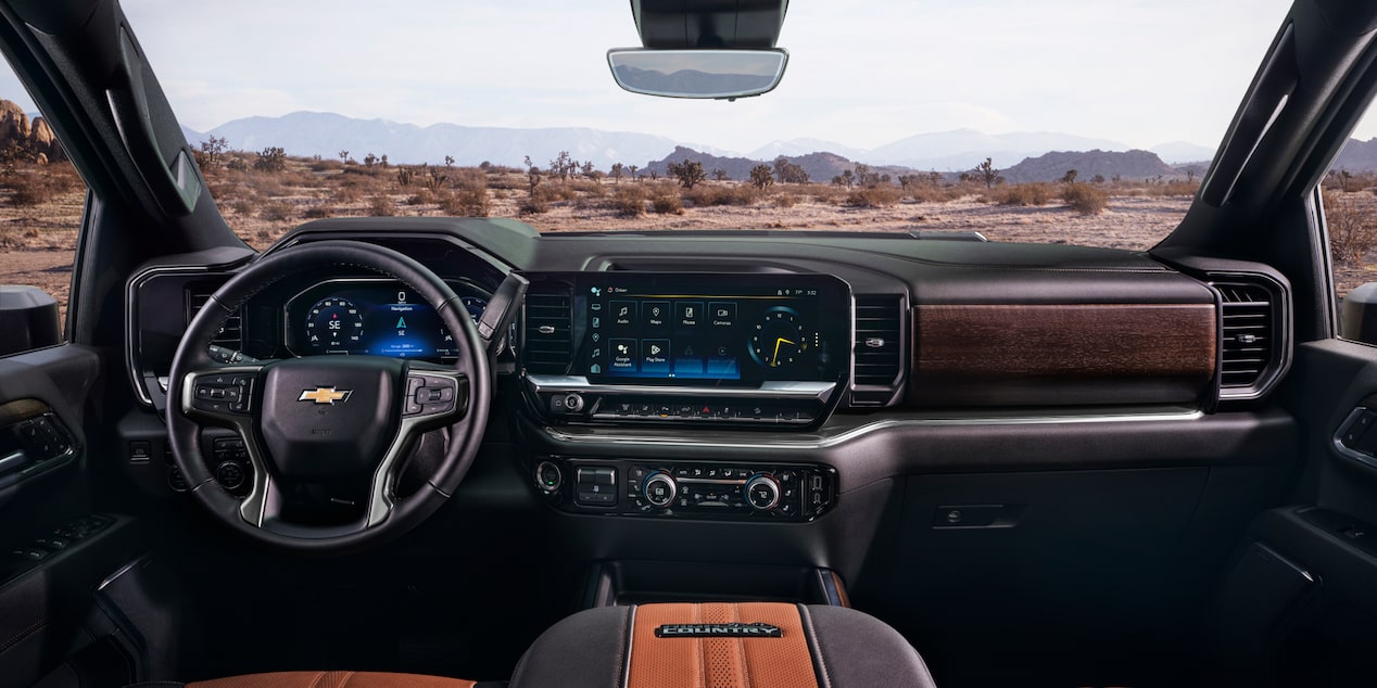 The Interior of a Chevy Silverado LD Featuring a Digital Dashboard, Leather Steering Wheel, and Center Touchscreen Display While Overlooking a Dirt Trail.
