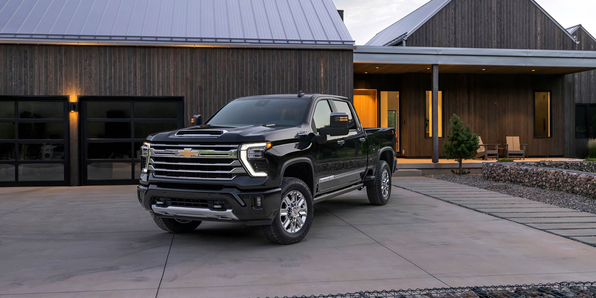 A black Chevrolet Silverado HD pickup parked in front of a modern barn-style house