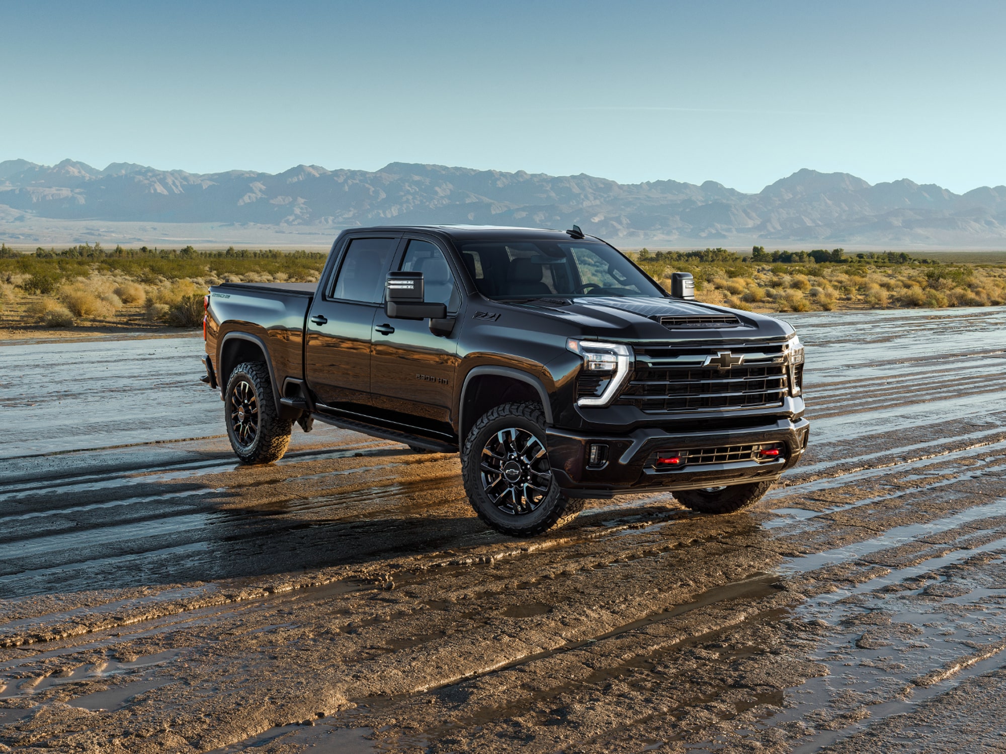 A White Chevrolet Silverado HD Stars and Steel Edition Truck on a Wet Dirt Road with Mountains.