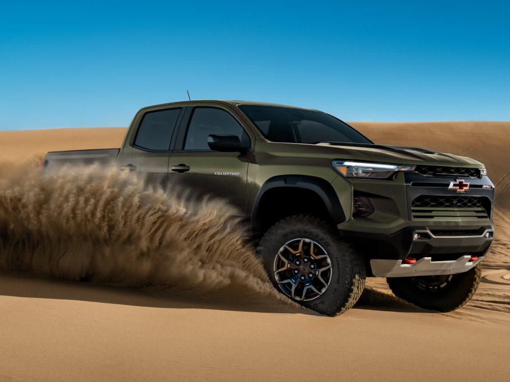 A Chevy Colorado Driving Through Sand With Dust and Debris Kicking Up Around the Truck.
