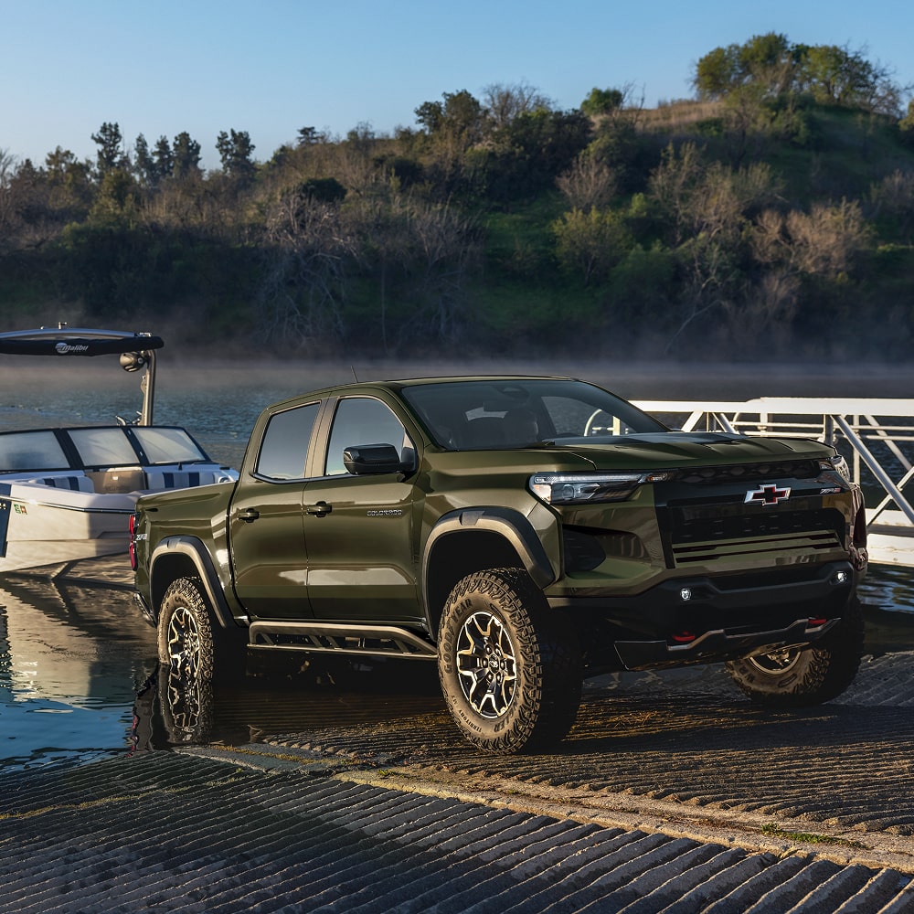 A Chevy Colorado Parked on a Boat Launch Ramp Beside a Lake With a Boat Trailer Attached.