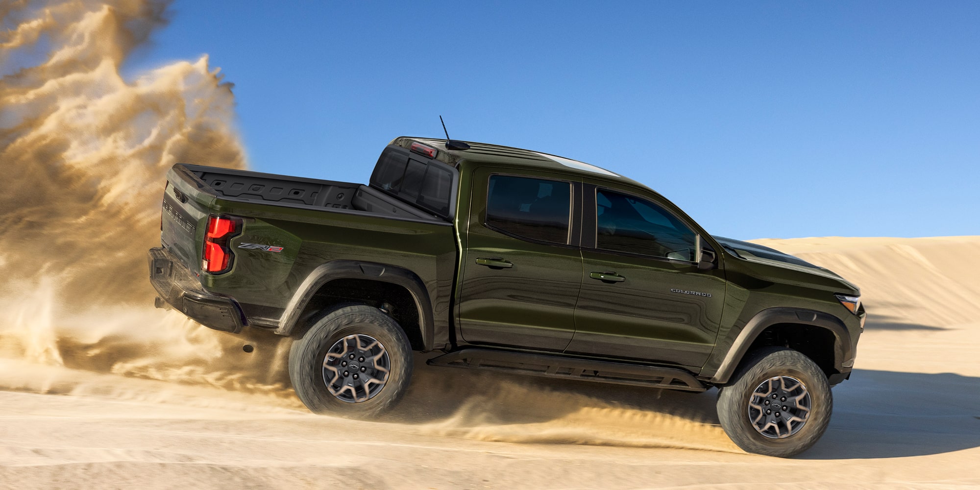 A Chevy Colorado Driving Across Sandy Terrain With a Large Cloud of Sand Trailing Behind the Truck.