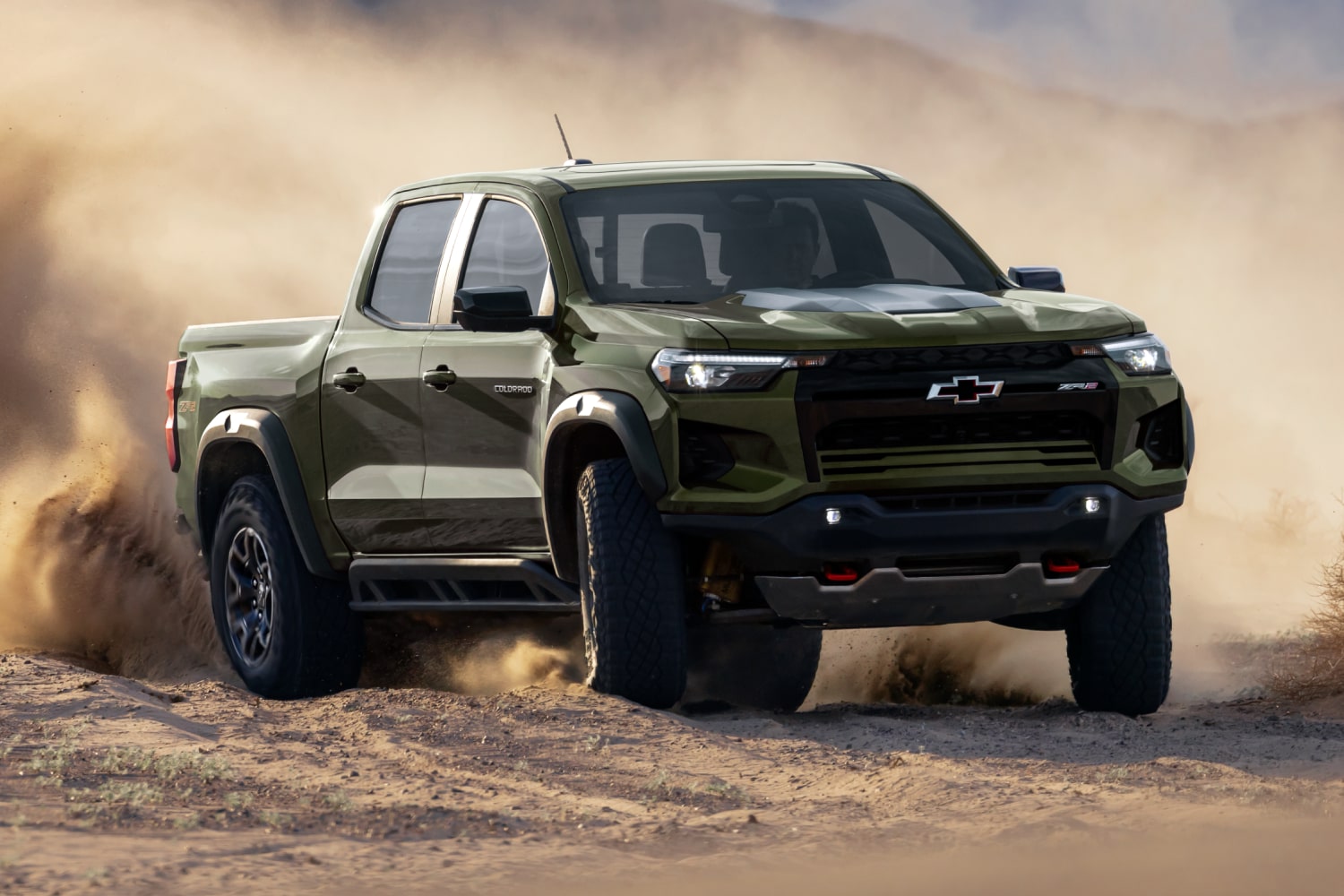 A Chevy Colorado Driving Through a Dusty Off-Road Trail With Dirt and Sand Kicking Up Around the Truck.