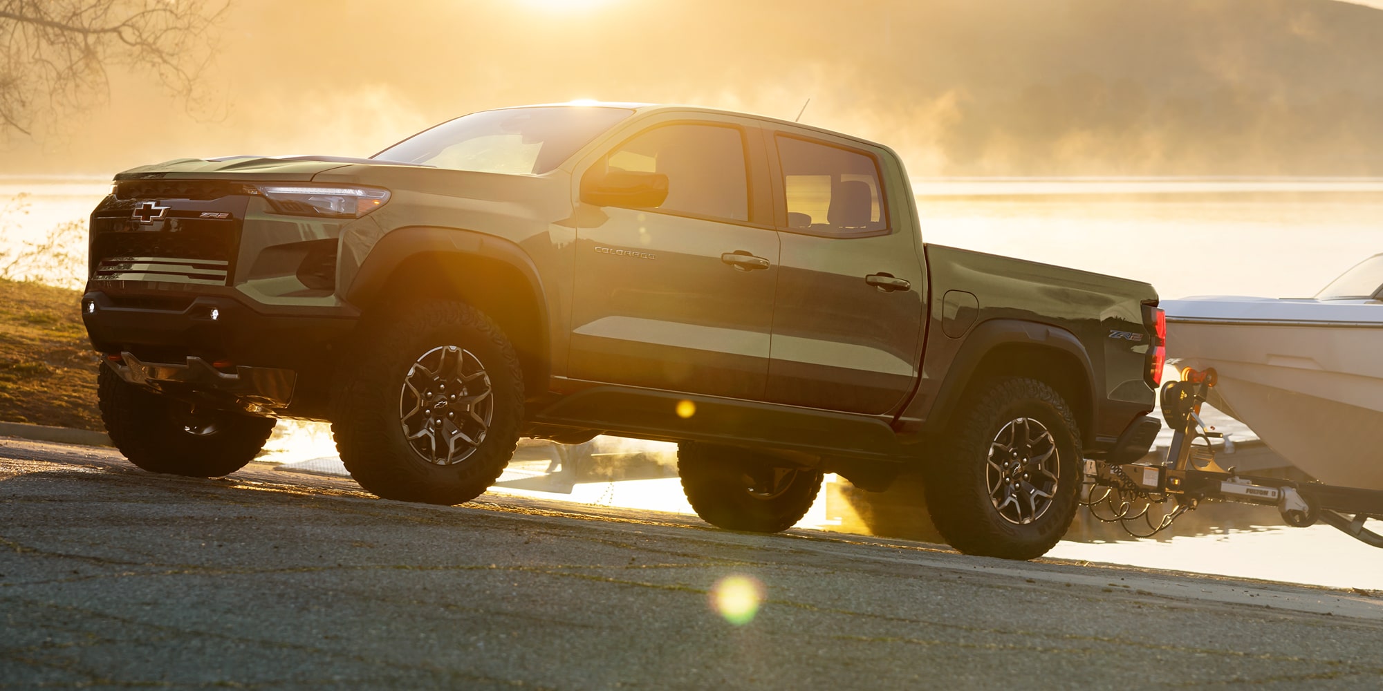 A Black Chevy Colorado Driving Through a Dusty Off-Road Trail at Sunset With Headlights Illuminated.