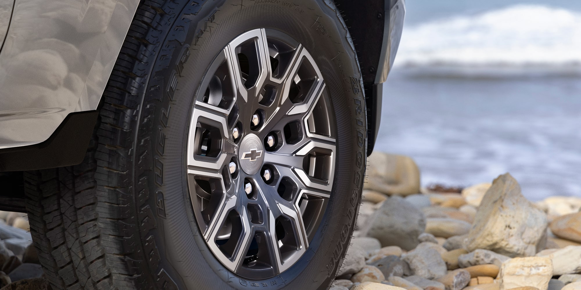 A Close-Up View of a Chevy Colorado Wheel and All-Terrain Tire Positioned on Rocky Terrain.